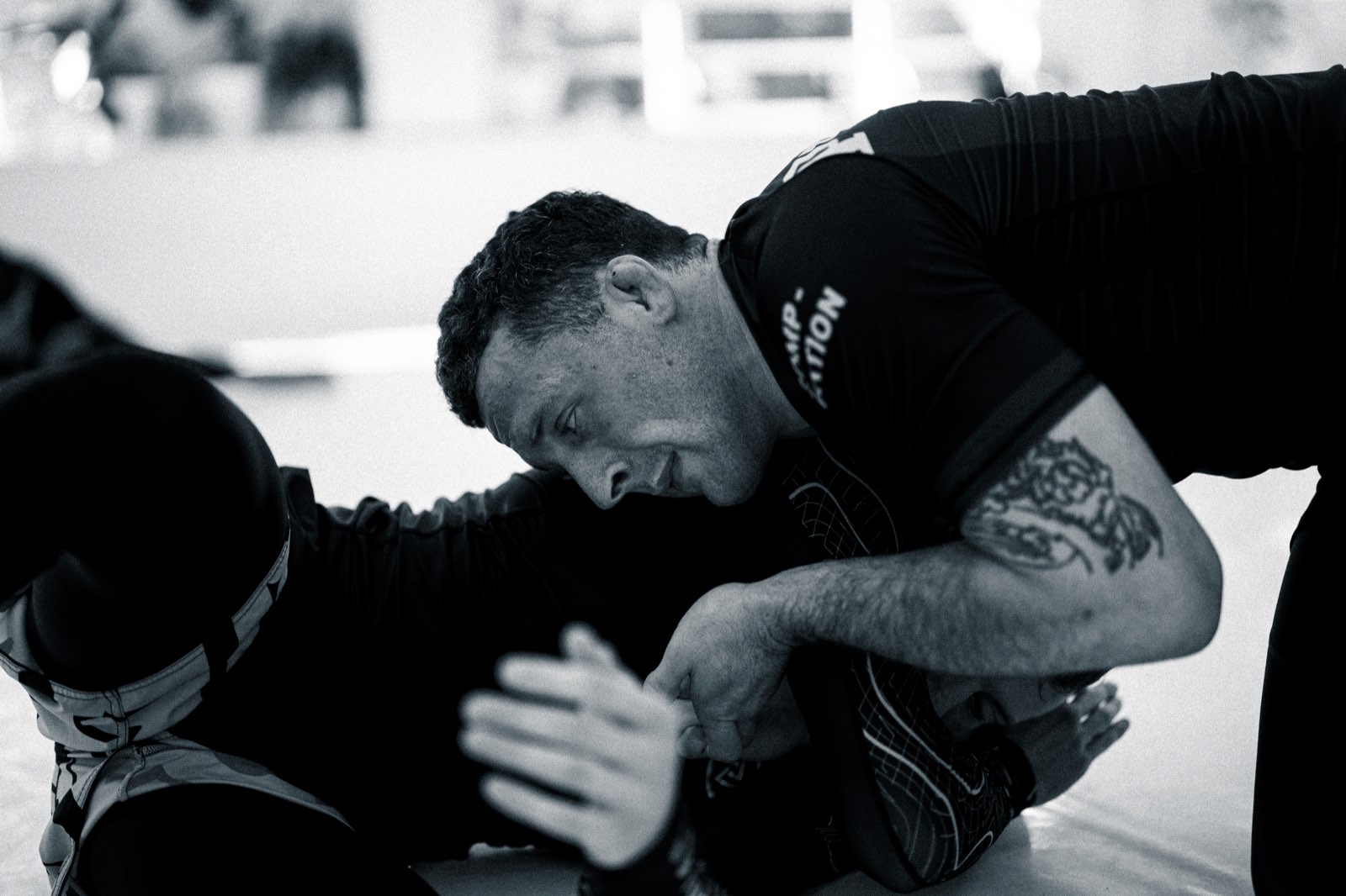 Sam in a rash guard on the mat, holding his partner's wrist and looking down at the grip